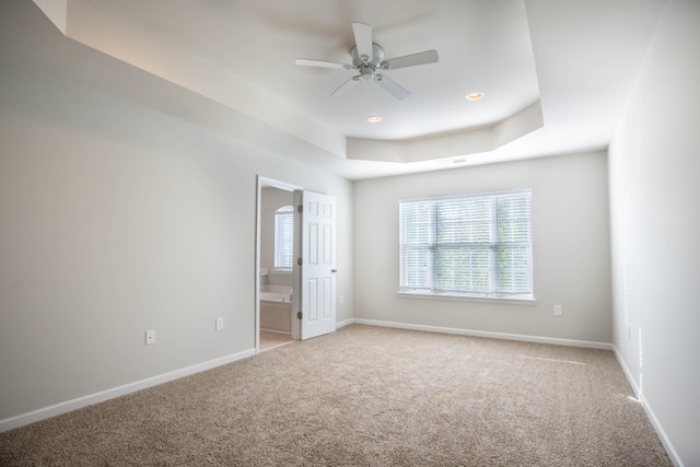 spare room with ceiling fan, a raised ceiling, and light colored carpet