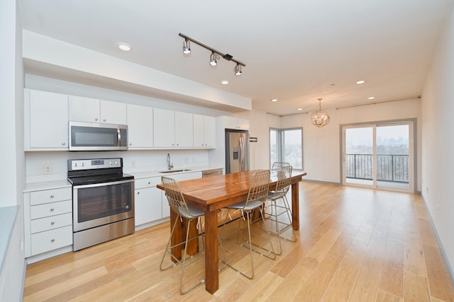 kitchen with white cabinets, sink, appliances with stainless steel finishes, decorative light fixtures, and light hardwood / wood-style floors