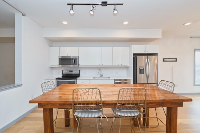 kitchen featuring appliances with stainless steel finishes, light wood-type flooring, track lighting, sink, and white cabinets