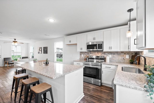 kitchen with a kitchen island, a sink, decorative backsplash, dark wood-type flooring, and stainless steel appliances
