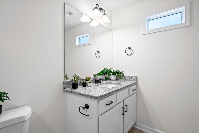 half bath with plenty of natural light, toilet, vanity, and baseboards