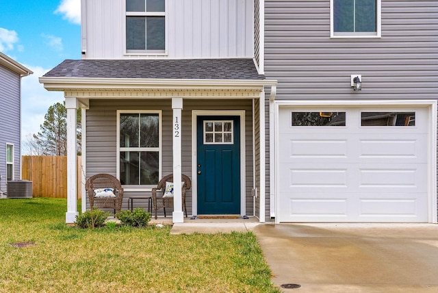 doorway to property featuring fence, a yard, covered porch, concrete driveway, and a shingled roof