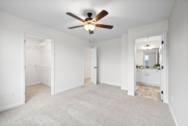 unfurnished bedroom featuring light carpet, a spacious closet, a closet, and baseboards