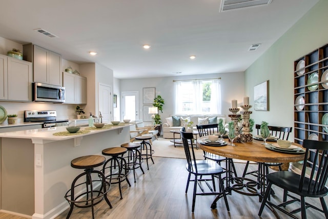 kitchen featuring gray cabinetry, stainless steel appliances, a kitchen bar, a kitchen island with sink, and light wood-type flooring