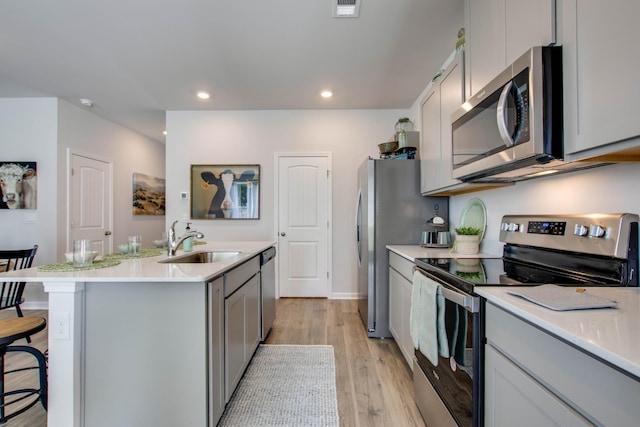 kitchen with a breakfast bar, a center island with sink, sink, light hardwood / wood-style flooring, and appliances with stainless steel finishes