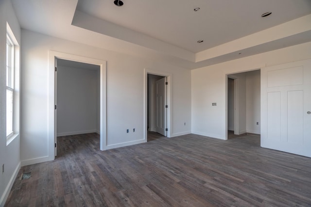 unfurnished bedroom featuring a raised ceiling, a spacious closet, and dark wood-type flooring