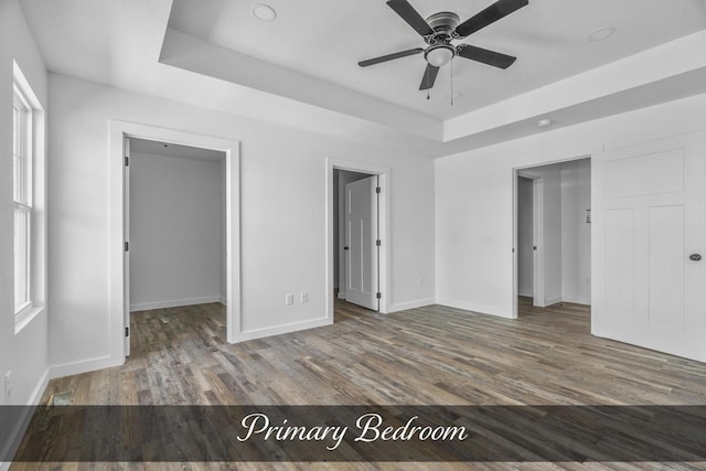 unfurnished bedroom with a tray ceiling, a spacious closet, and wood finished floors