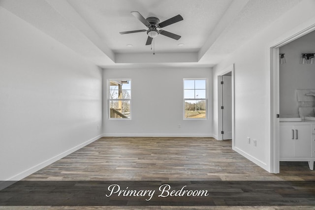 spare room with a raised ceiling, ceiling fan, baseboards, and wood finished floors