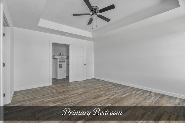 unfurnished bedroom featuring ceiling fan, baseboards, a raised ceiling, and dark wood finished floors