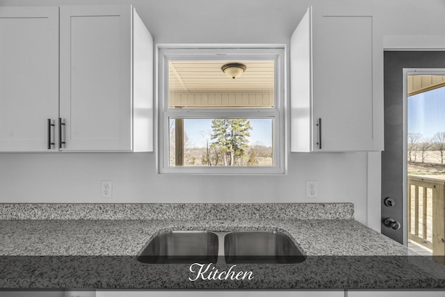 kitchen featuring light stone counters, a sink, and white cabinetry