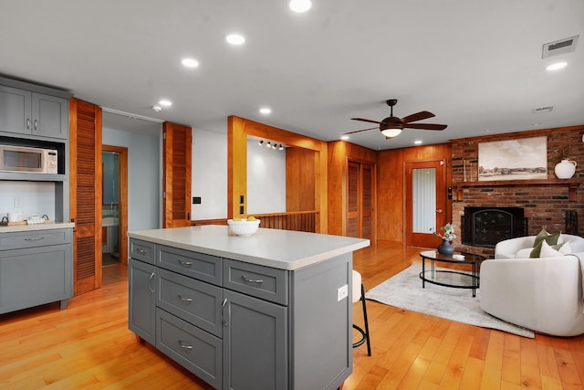 kitchen with light wood-type flooring, ceiling fan, a fireplace, gray cabinets, and a kitchen island