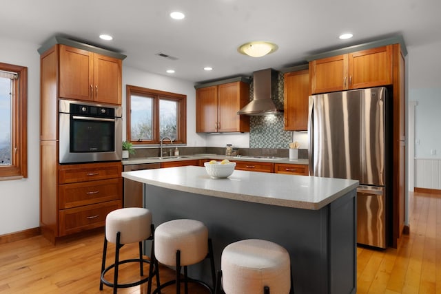 kitchen with a kitchen breakfast bar, a kitchen island, wall chimney range hood, and appliances with stainless steel finishes