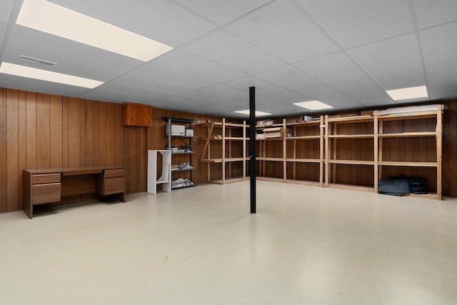 basement with a paneled ceiling and wood walls