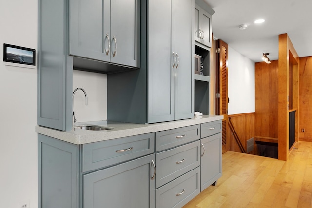 kitchen with gray cabinetry, wooden walls, sink, and light hardwood / wood-style flooring