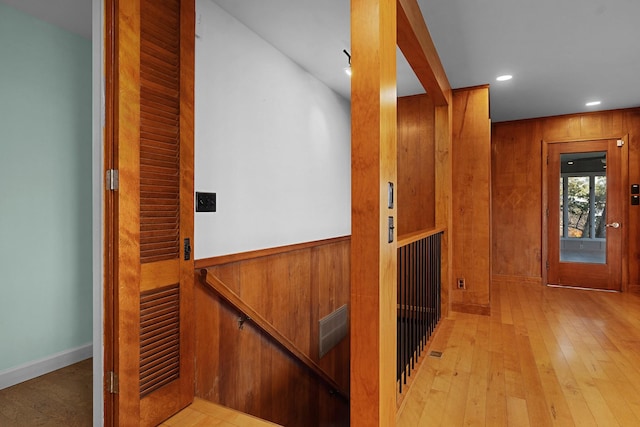 corridor featuring light wood-type flooring and wooden walls