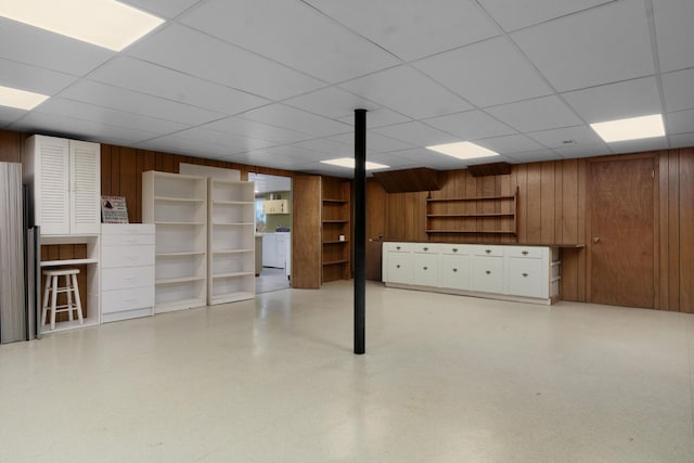 basement featuring a drop ceiling and wood walls