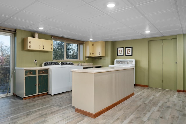 clothes washing area with washer and dryer, light wood-type flooring, and cabinets