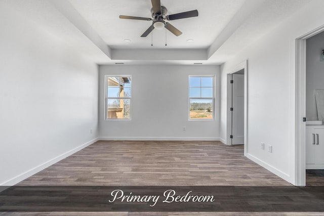 spare room featuring wood finished floors, a raised ceiling, a ceiling fan, and baseboards