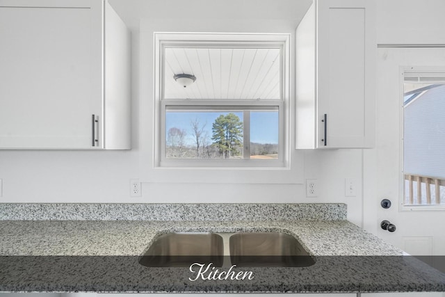 kitchen with light stone countertops, white cabinets, and a sink