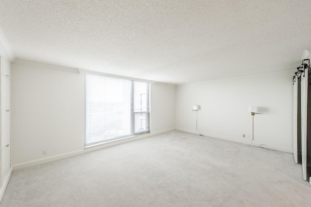 empty room with light carpet, a textured ceiling, a barn door, and ornamental molding