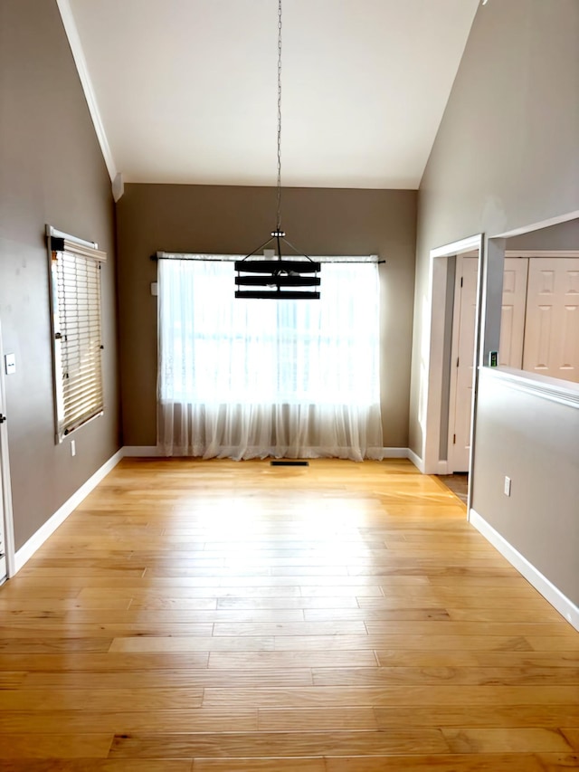 unfurnished dining area with a notable chandelier, lofted ceiling, and light hardwood / wood-style flooring