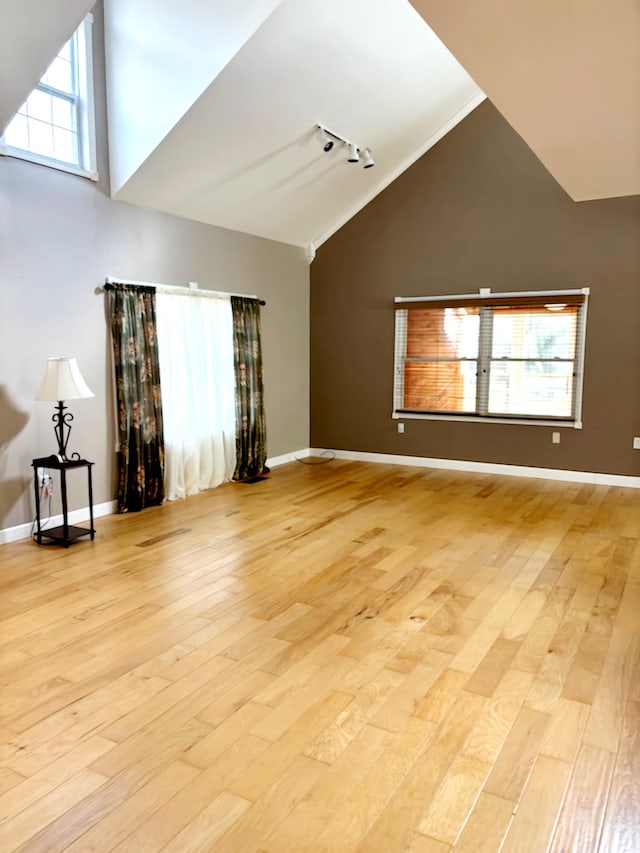 unfurnished living room featuring track lighting, light hardwood / wood-style floors, and vaulted ceiling