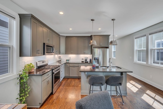 kitchen featuring decorative backsplash, gray cabinetry, stainless steel appliances, pendant lighting, and hardwood / wood-style floors