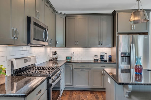 kitchen with hanging light fixtures, stainless steel appliances, dark hardwood / wood-style flooring, dark stone countertops, and gray cabinets