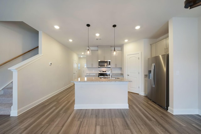 kitchen with light stone countertops, dark wood-type flooring, hanging light fixtures, a center island with sink, and appliances with stainless steel finishes