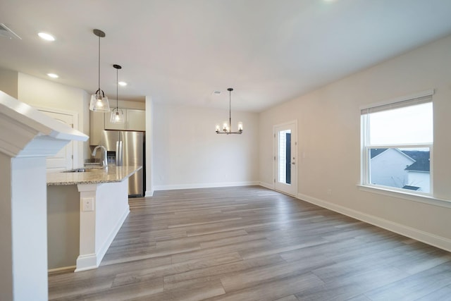 kitchen featuring pendant lighting, an inviting chandelier, stainless steel fridge, light stone countertops, and wood-type flooring