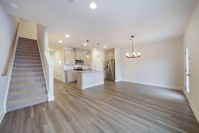 kitchen featuring stainless steel appliances, light hardwood / wood-style flooring, an island with sink, decorative light fixtures, and white cabinets