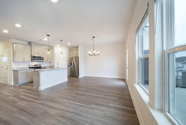 kitchen with stainless steel appliances, a kitchen island with sink, decorative light fixtures, light hardwood / wood-style flooring, and a notable chandelier