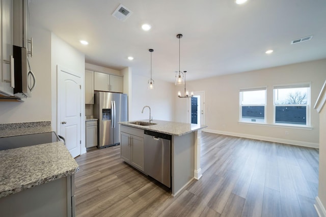 kitchen featuring gray cabinetry, sink, light stone countertops, an island with sink, and appliances with stainless steel finishes