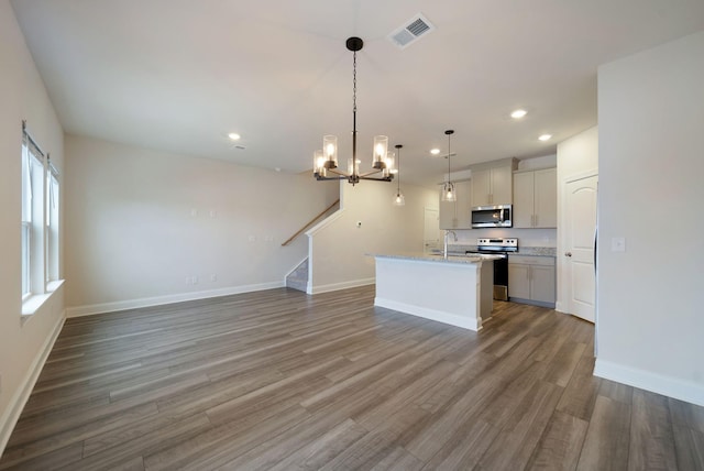 kitchen featuring sink, hardwood / wood-style flooring, an island with sink, decorative light fixtures, and stainless steel appliances