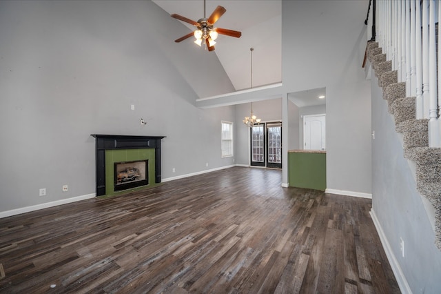 unfurnished living room featuring french doors, ceiling fan with notable chandelier, dark wood-type flooring, high vaulted ceiling, and a tiled fireplace