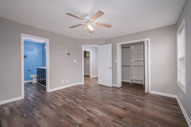 unfurnished bedroom with ensuite bath, ceiling fan, dark wood-type flooring, multiple windows, and a closet