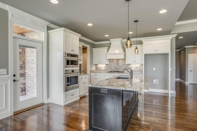 kitchen with a kitchen island with sink, pendant lighting, custom range hood, and white cabinets