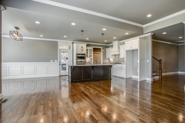 kitchen with a kitchen breakfast bar, custom range hood, white cabinets, decorative light fixtures, and a large island with sink