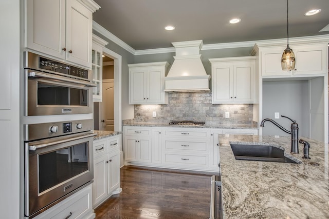 kitchen with sink, white cabinetry, custom range hood, pendant lighting, and stainless steel appliances