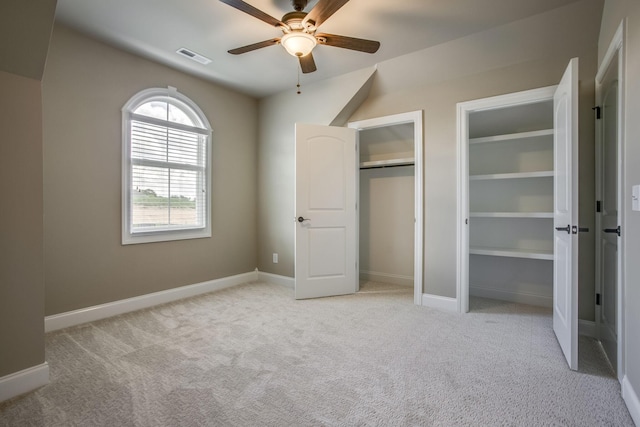 unfurnished bedroom featuring two closets, light colored carpet, and ceiling fan