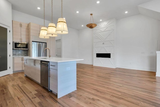 kitchen with pendant lighting, a center island with sink, light brown cabinetry, tasteful backsplash, and stainless steel appliances