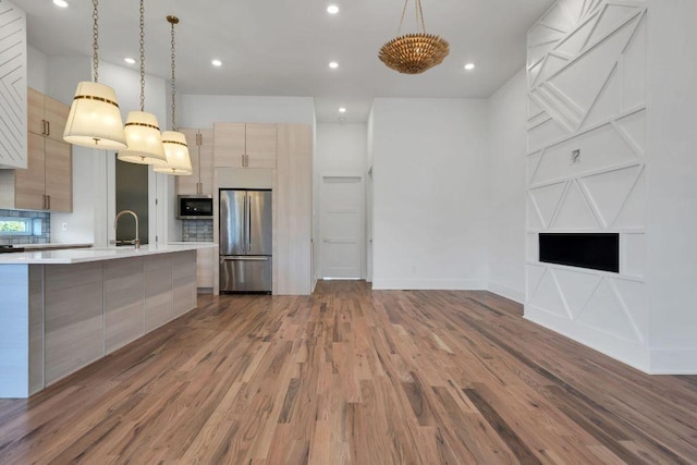 kitchen featuring tasteful backsplash, stainless steel appliances, light brown cabinets, hardwood / wood-style floors, and hanging light fixtures