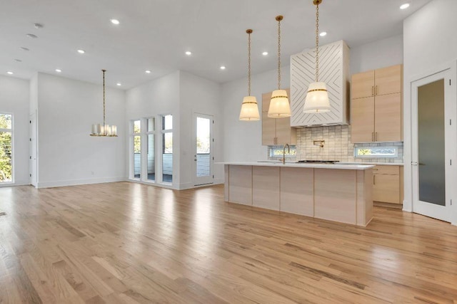 kitchen with backsplash, a kitchen island with sink, light brown cabinets, and hanging light fixtures