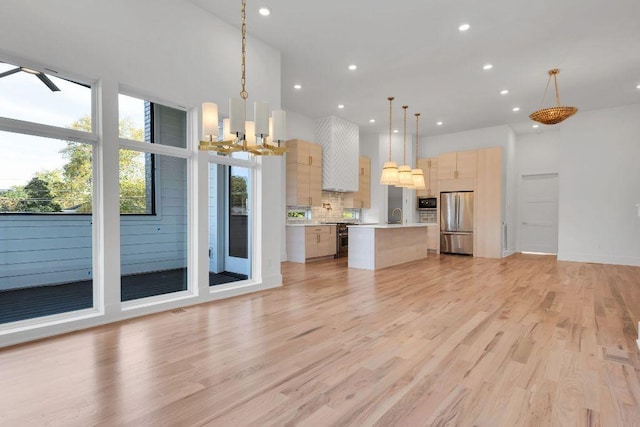 kitchen with tasteful backsplash, stainless steel appliances, light brown cabinets, a kitchen island, and hanging light fixtures