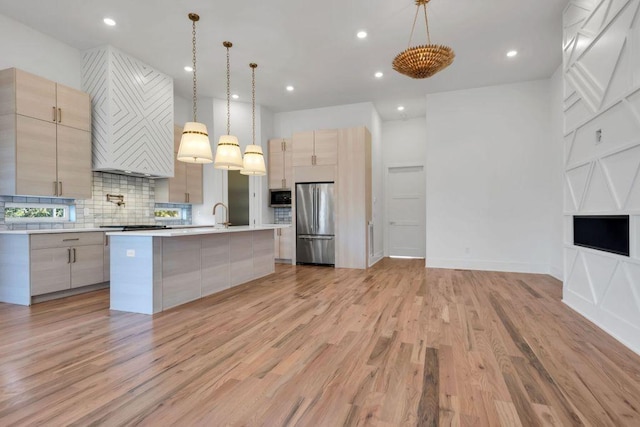 kitchen featuring backsplash, an island with sink, light brown cabinetry, decorative light fixtures, and stainless steel appliances