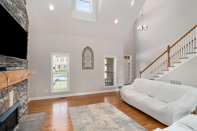 living room featuring an inviting chandelier, a stone fireplace, light wood-type flooring, and a high ceiling