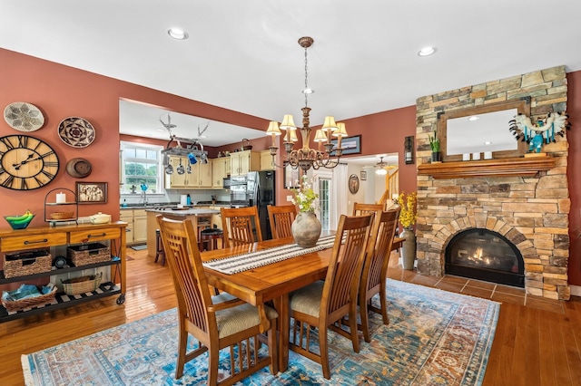 dining space with a stone fireplace, light hardwood / wood-style flooring, and a notable chandelier