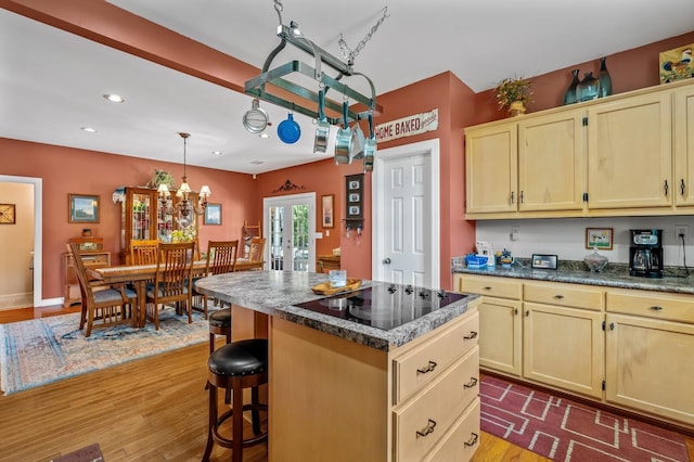 kitchen featuring an inviting chandelier, hardwood / wood-style floors, pendant lighting, black electric cooktop, and a kitchen island