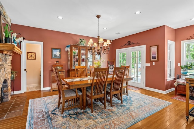 dining area with hardwood / wood-style floors, a notable chandelier, a fireplace, and french doors