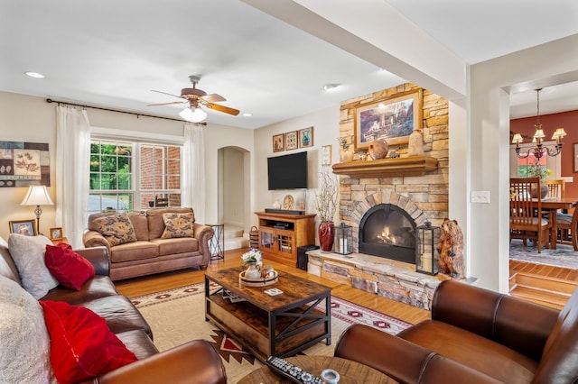 living room featuring ceiling fan with notable chandelier, hardwood / wood-style flooring, and a stone fireplace